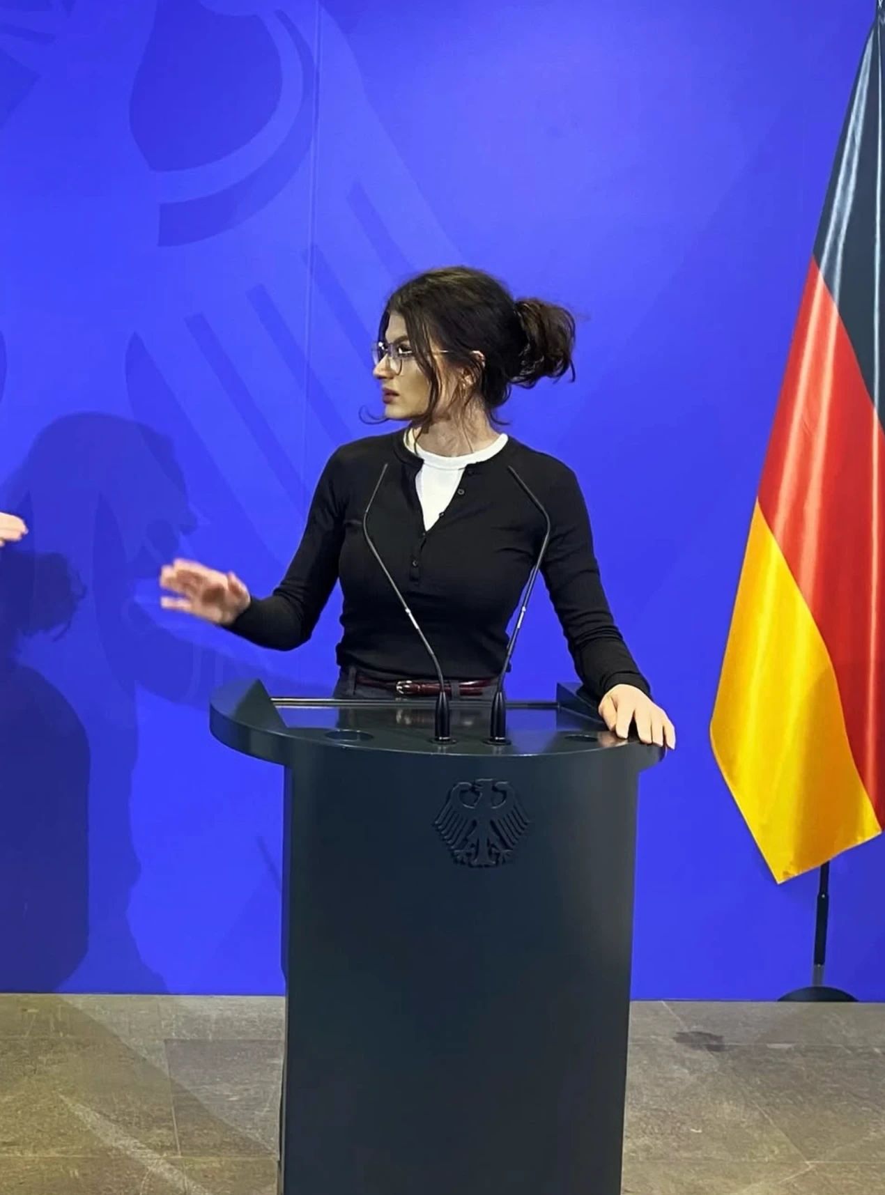 Linda Loran am Rednerpult vor blauer Wand mit Bundesadler und Deutschlandflagge
